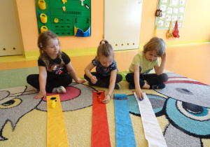 Dzieci układają kolorowe misie zgodnie z liczbą na wstążce wiatraka.